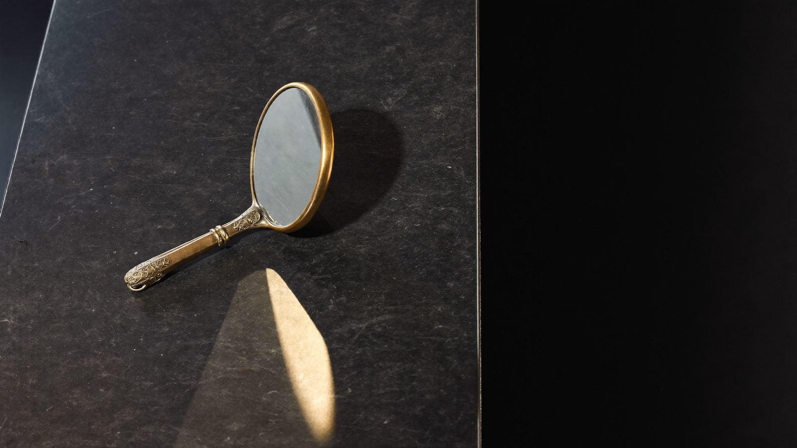 An antique brass hand mirror on dark stone — examining your marketing agency
