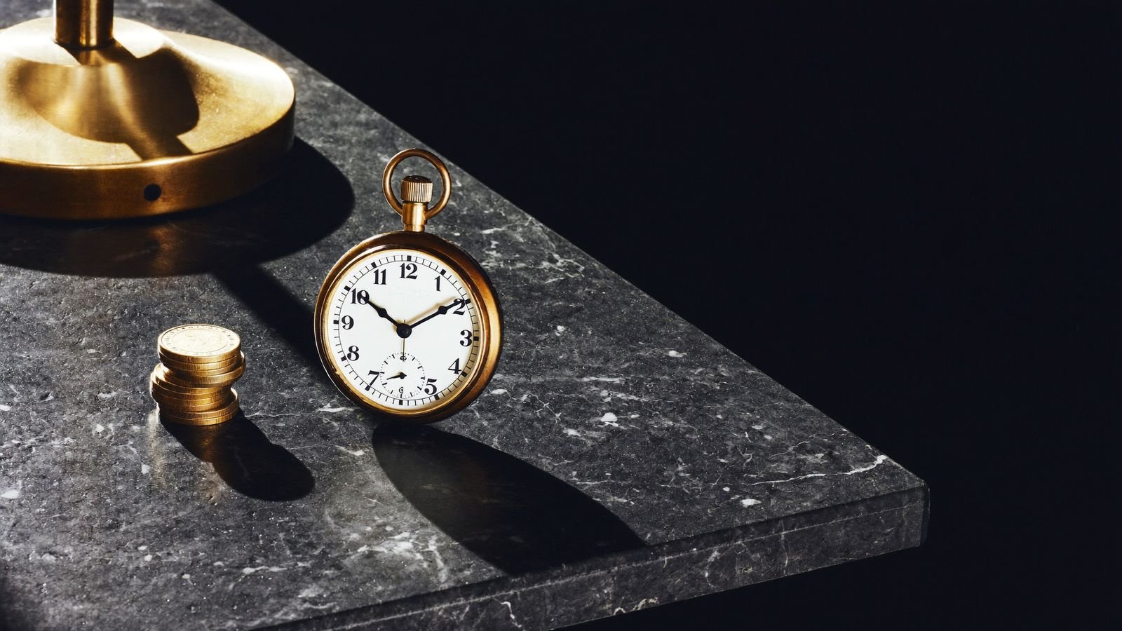 A stopped pocket watch and an untouched stack of coins on dark stone, representing a Meta ads budget that is not spending